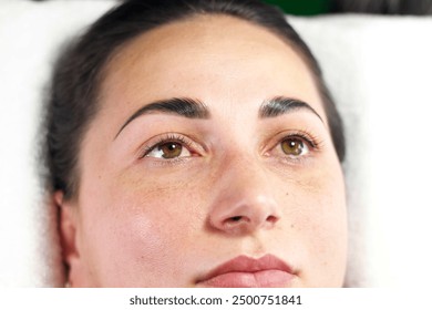 A woman lying on a treatment bed with freshly tinted eyebrows. Her eyes are open, showcasing the results of the beauty procedure.  - Powered by Shutterstock