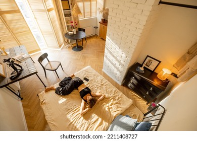 Woman Lying Relaxed On Bed In Beautiful And Sunny Studio Apartment, View From Above