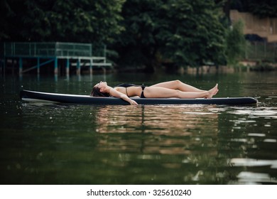 woman lying and relaxing on a paddle board on a lake surrounded by trees