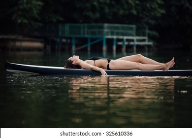 woman lying and relaxing on a paddle board on a lake surrounded by trees
