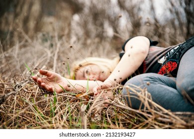 Woman lying unconscious in the autumn grass. Selective focus on hands. Close up dead female person in nature