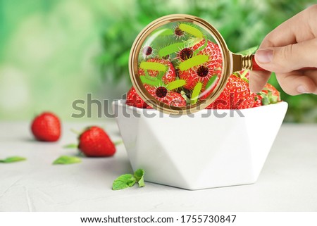 Woman with magnifying glass detecting microbes on strawberries, closeup. Food poisoning concept  
