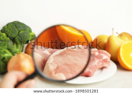 Woman with magnifying glass exploring raw meat and fruits, closeup. Poison detection