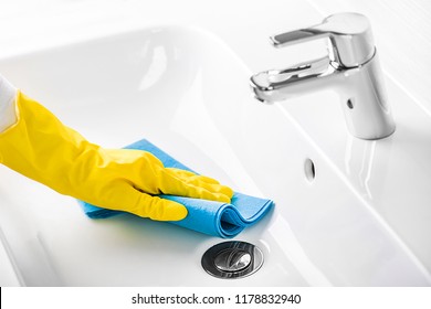 Woman maid or charwoman cleaning modern new basin in bathroom, water tap clean using yellow gloves and blue cloth.