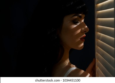 Woman With Make Up And Red Lips Looks At Jalousie. Sexy, Desire, Fashion, Romance, Morning Concept. Girl With Sensual Face And Beautiful Breasts. Sexy Girl With Long Dark Hair. Light And Shadow.