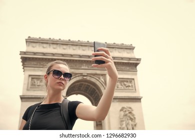 Woman make selfie with phone at arc de triomphe in paris, france. Woman with smartphone at arch monument. Vacation and sightseeing in french capital. Girl with fashion look and sensual beauty.