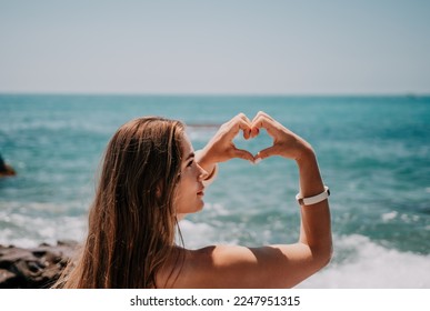Woman makes heart with hands on beach. Young woman with long hair in white swimsuit and boho style braclets practicing by sea ocean. Concept of longing daydreaming love peace contemplation vacations - Shutterstock ID 2247951315