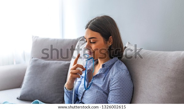 Woman makes inhalation nebulizer at home.\
Holding a mask nebulizer inhaling fumes spray the medication into\
your lungs sick patient. Self-treatment of the respiratory tract\
using inhalation\
nebulizer