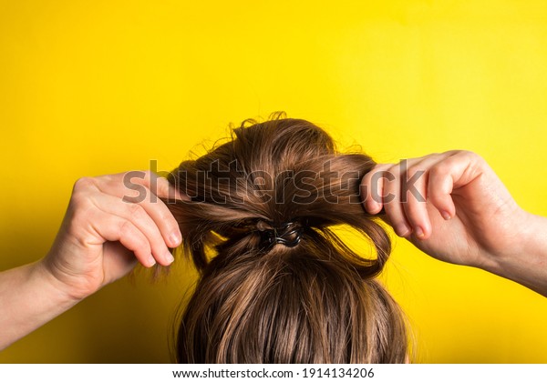 A woman makes a messy\
hair bun on her head. Yellow background. Copy space. Trend color of\
the year 2021