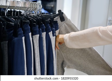 woman makes purchases, goes through a row of identical clothes on hangers in the store, sweatpants, concept of fashion, shopping, seasonal sales, prices for mass consumption goods