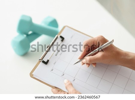 Woman makes workout plan for week next to dumbbells. Daily sports and healthy lifestyle concept