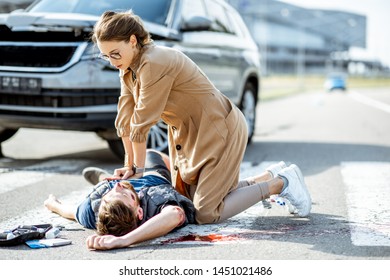 Woman making artificial respiration to the injured bleeding man lying on the pedestrian crossing after the road accident