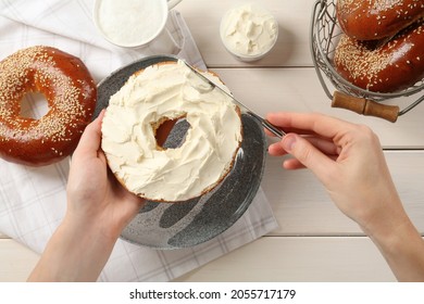 Woman Making Bagel With Cream Cheese At White Wooden Table, Top View