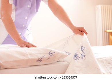 Woman Making Bed And Changing Bedding In Guest Room.