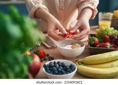 Woman Making Bowl Full Of Yogurt With Strawberries 