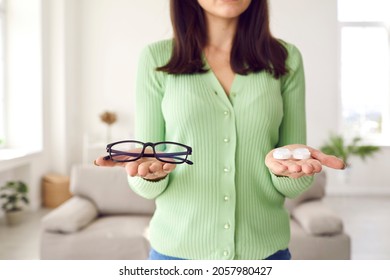 Woman making choice between glasses and eye lenses. Young girl who's holding eyeglasses and container box with pack of modern color lenses is trying to choose which to wear. Cropped shot, close up