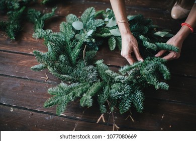 Woman making christmas wreath on a dark wooden table. Concept of florist's work before christmas holidays. - Shutterstock ID 1077080669