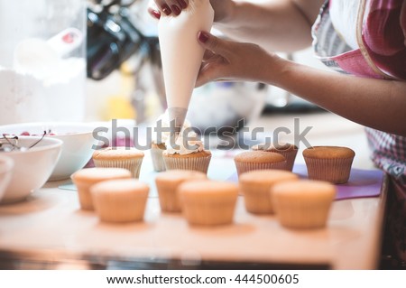Woman making creamy top of cupcakes closeup. Selective focus.