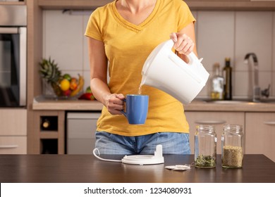 Woman making a cup of tea in the morning, pouring a boiling water from a kettle into a cup - Powered by Shutterstock