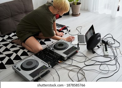 Woman making electronic music on laptop computer and digital instruments while sitting at the floor at home. Young female producing modern indie music on synthesizer and digital controllers