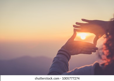 Die Frau, die mit ihren Händen im Sonnenaufgang einen Rahmen um die Sonne bildet, Kopienraum, warmer Retro-Ton.