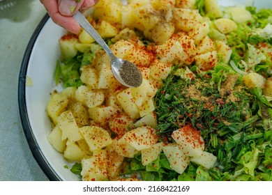 Woman making fresh and delicious potato salad filled with greens on a tray, pouring black pepper from a small plate onto the salad. Turkish cuisine. - Shutterstock ID 2168422169