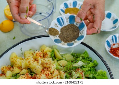 Woman Making Fresh And Delicious Potato Salad Filled With Greens On A Tray, Pouring Black Pepper From A Small Plate Onto The Salad. Turkish Cuisine.