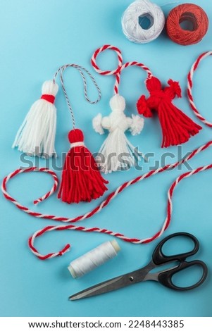 Woman making handmade traditional martisor, from red and white strings with tassel. Symbol of holiday 1 March, Martenitsa, Baba Marta, beginning of spring in Romania, Bulgaria, Moldova
