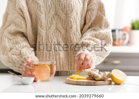 Woman making healthy tea with ginger and lemon in kitchen