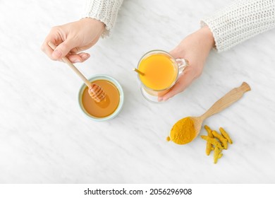 Woman Making Healthy Turmeric Drink With Honey On Light Background