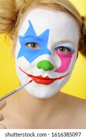 Woman is making up her face as a clown for carnival or halloween