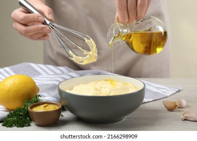 Woman making homemade mayonnaise in ceramic bowl at wooden table, closeup