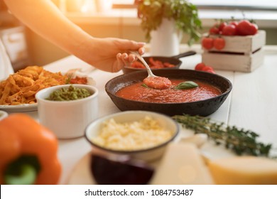 Woman Making Homemade Pasta With Tomato Sous And Cheese Over Old Wooden Table. Tomato, Olive Oil, Spices, Herbs, Cheese, Tomato Sauce On A Weathered Wooden Table In The Summer Sun's Rays. Organic Food