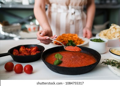 Woman Making Homemade Pasta With Tomato Sous And Cheese Over Old Wooden Table. Tomato, Olive Oil, Spices, Herbs, Cheese, Tomato Sauce On A Weathered Wooden Table In The Summer Sun's Rays. Organic Food