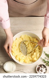 Woman making mashed potato at wooden table, top view