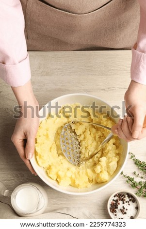 Woman making mashed potato at wooden table, top view