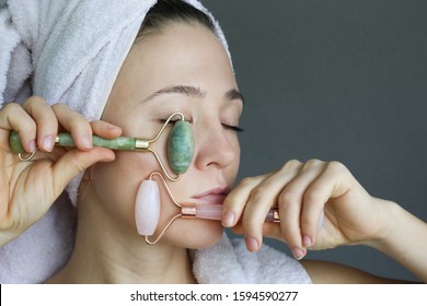  Woman making massage with green jade roller. Beauty tools for face treatment. Funny face.