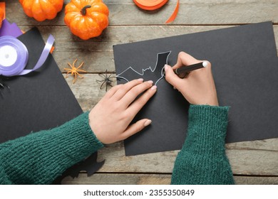 Woman making paper bats for Halloween on brown wooden background