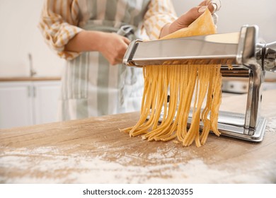 Woman making pasta with machine at table in kitchen, closeup - Powered by Shutterstock