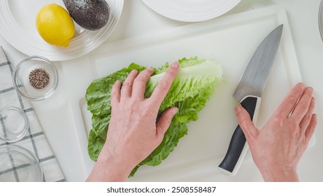 Woman making Romaine lettuce celery salad. Leaves of fresh green lettuce close-up on a white cutting board, flat lay - Powered by Shutterstock