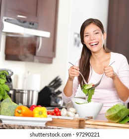 Woman Making Salad In Kitchen Smiling And Laughing Happy And Cheerful. Beautiful Young Multiracial Caucasian / Chinese Asian Young Woman At Home.