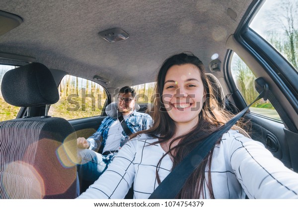 woman making selfie while driving car with\
sitting man on backseats. car travel\
concept