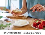 Woman making summer strawberry sandwich. Female hands spread stracchino cheese on bread for toast. Healthy eating, fruit dieting brunch.