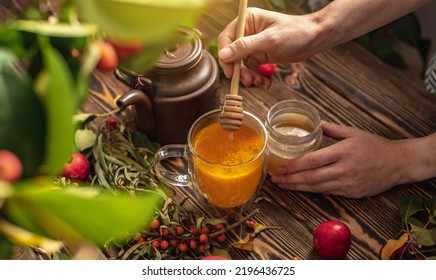 Woman Is Making A Tasty And Healthy Vitamin Tea From Fresh Sea Buckthorn Berries With Honey. Concept Of A Cozy Autumn Atmosphere And Health Care During Colds And Flu Season.