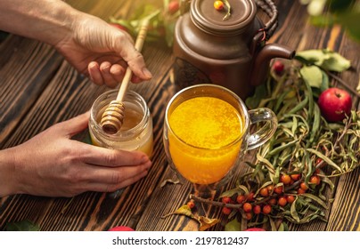 Woman Is Making A Tasty And Healthy Vitamin Tea From Fresh Sea Buckthorn Berries With Honey. Concept Of A Cozy Autumn Atmosphere And Health Care During Colds And Flu Season.