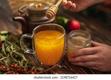 Woman Is Making A Tasty And Healthy Vitamin Tea From Fresh Sea Buckthorn Berries With Honey. Concept Of A Cozy Autumn Atmosphere And Health Care During Colds And Flu Season.