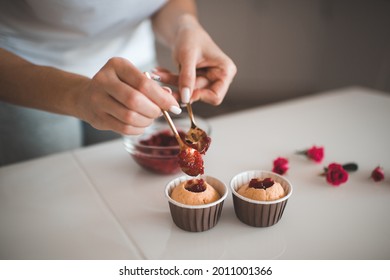 Woman making tasty muffins with fruit jam filling on kitchen table indoors at home. Girl baking cup cakes with strawberry in it. Vegan pastry.  - Powered by Shutterstock