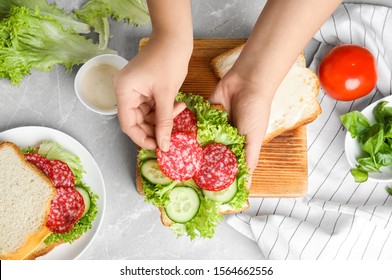 Woman Making Tasty Sandwich At Light Grey Marble Table, Top View