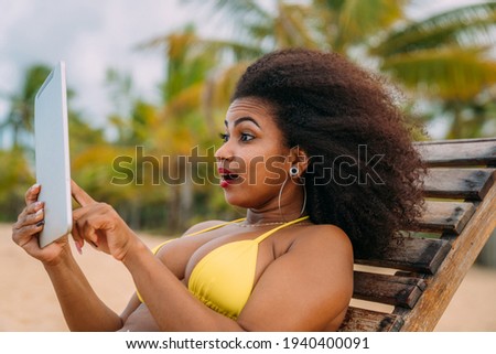 Woman making a video call on summer vacation. latin american woman sitting on the beach chair with a tablet
