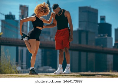 A woman and a man in athletic wear stretching before a workout in an urban setting, with skyscrapers in the background - Powered by Shutterstock